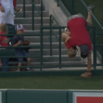 Guy holding a toddler reaches over rail to grab a baseball and nearly finds disaster instead